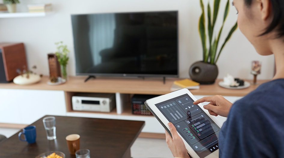 Une femme ajuste les paramètres de sa tablette pour illustrer comment utiliser la technologie intelligente pour la maison.