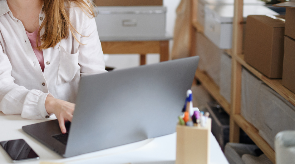 A person works on a laptop in a storeroom, preparing an emergency plan for their small business.