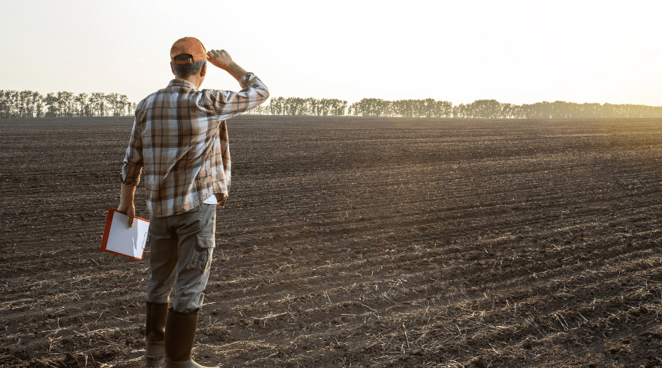 A farmer stands in his field with a clipboard, showing how he prepares his farm for wildfire season to reduce damage