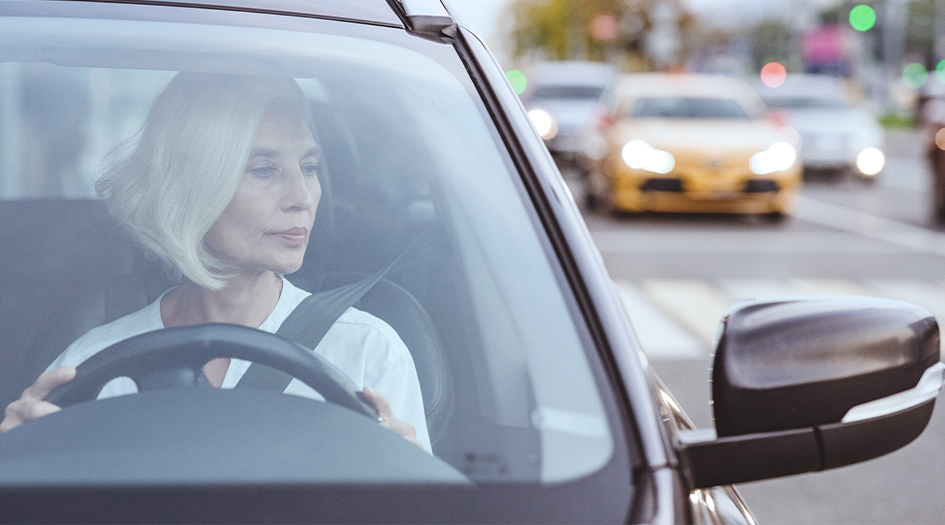 A woman checks her side mirror while driving, as she wonders what accident forgiveness means in a car insurance policy