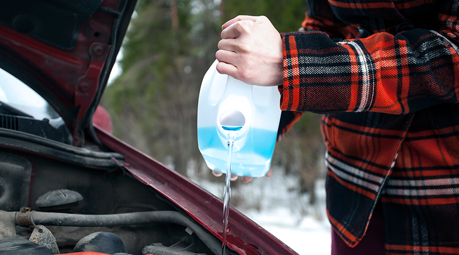 Here are some tips for a safe winter road trip, as shown by someone pouring windshield washer fluid into their car