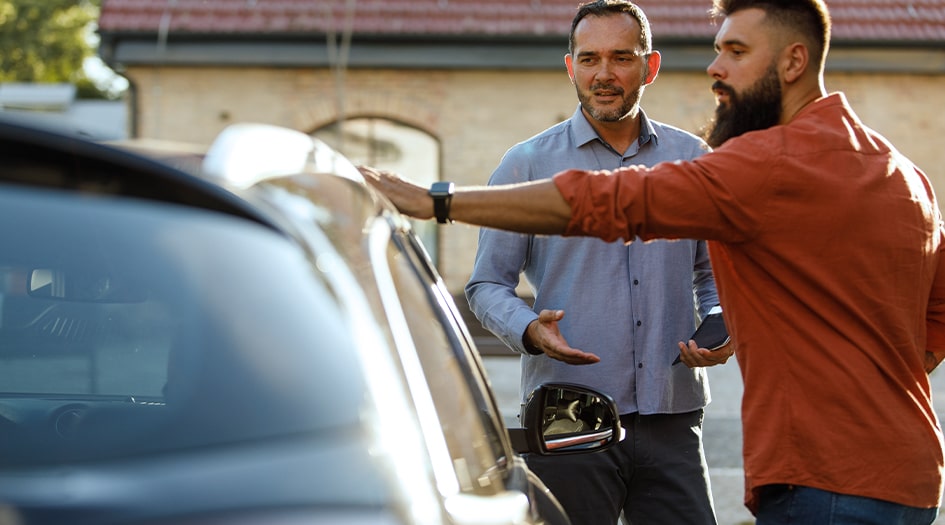 A man looks at a car with a salesman as he asks questions to avoid buying a stolen car