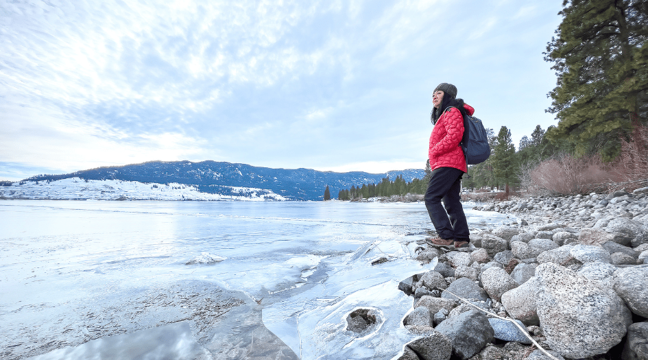 A woman looks out at a frozen lake, showing one precaution to take before going on the ice.