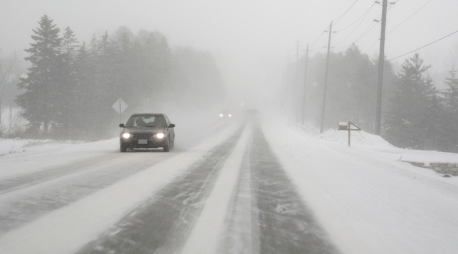 Des voitures roulent prudemment sur une route enneigée à faible visibilité en raison du brouillard givrant.