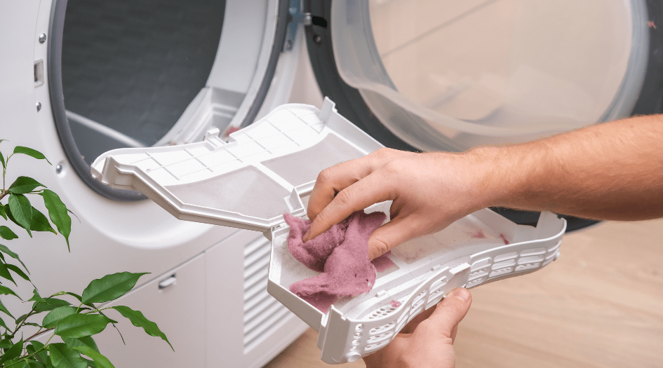 Someone removing lint from their dryer shows one essential maintenance task you need to do for your major home appliances.