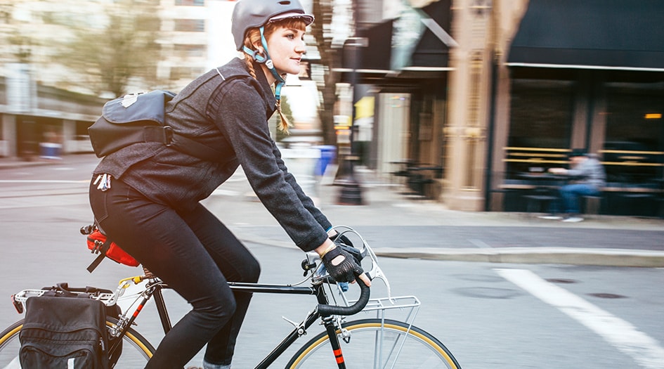 Une femme portant un casque et un manteau fait du vélo dans une rue afin de montrer comment faire du vélo l’été en toute sécurité.