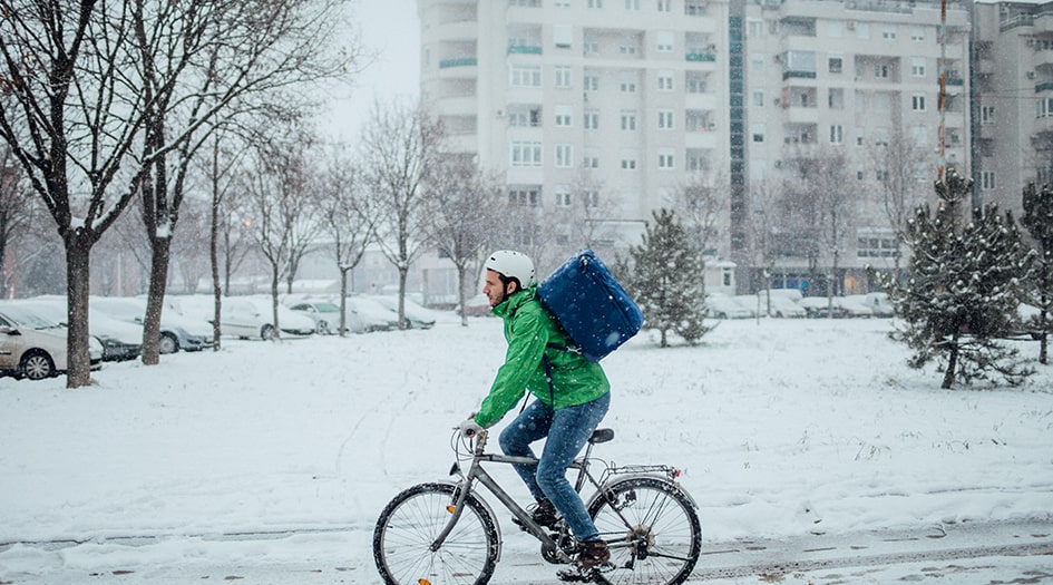 Un homme roule à vélo dans la neige en respectant le guide pour faire du vélo l’hiver en toute sécurité.