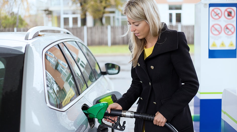 A woman fills up her car with gas, showing you how to navigate rising gas prices and drive for fuel efficiency 