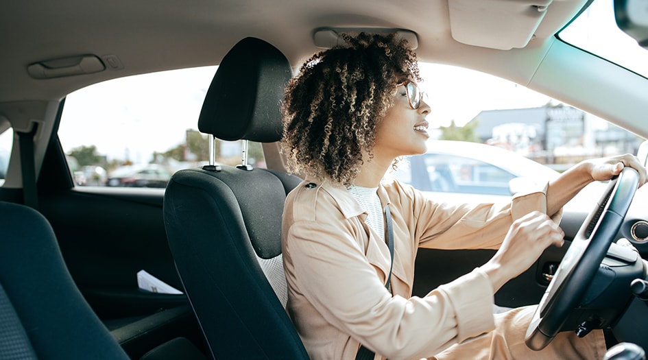 Une femme avec des lunettes et un manteau conduit une voiture et se demande si elle peut laisser quelqu’un conduire sa voiture.