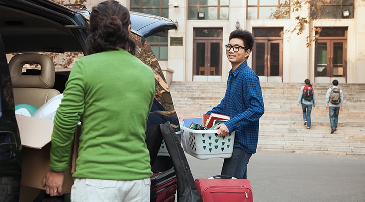 A mother helps her son unload the car as they move him into his school dorm, following the key steps to prepare him for dorm life