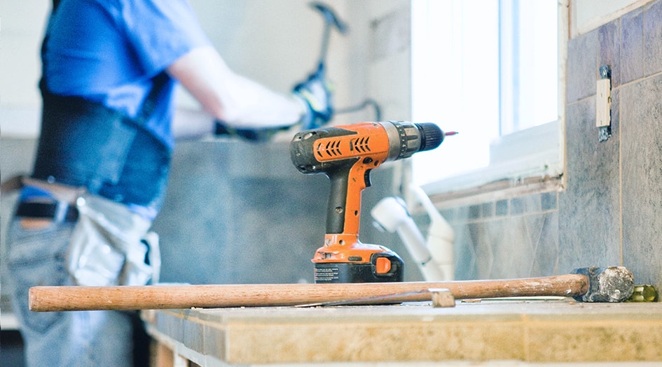 A man hammers in the background with a sledgehammer and drill in front of him, showing why it's important to hire a licensed contractor