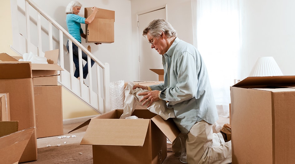 An elderly man and woman pack up cardboard boxes in their home as they prepare to downsize their house