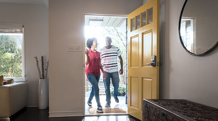 A man and woman walk into the open front door of their house as they follow a few key steps for first-time homebuyers