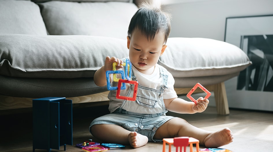 A small baby plays with interlocking blocks on the floor, showcasing why you need to baby proof your home