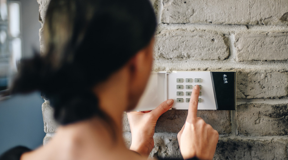 A woman types in a code into her home security system, showing one way to make your home more secure 