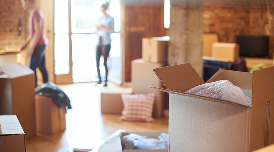 Un homme et une femme entourés de boîtes déballent leurs biens et suivent les conseils pour propriétaires d’une première maison.