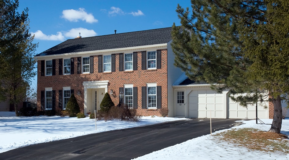 A large brown house appears uninhabited with snow around it, showing you why you need to keep your home safe when you head down south for the winter