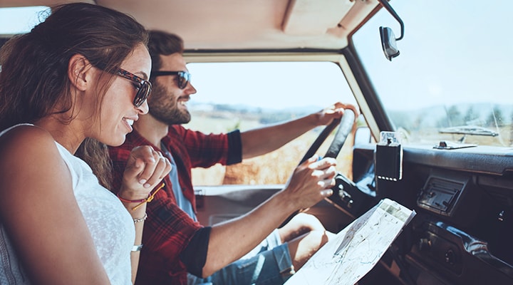 Follow these 10 tips for a safer road trip, as shown by a man and woman checking a map while in the front seat of a car