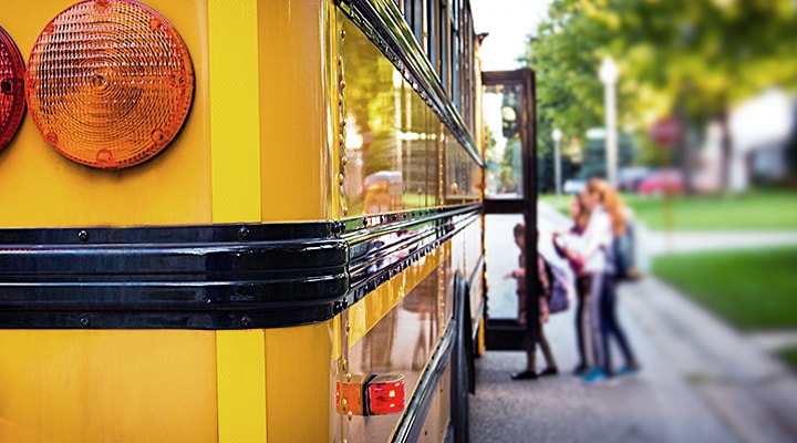 Trois enfants montent dans l’autobus scolaire, ce qui montre pourquoi il faut conduire prudemment à la rentrée des classes.