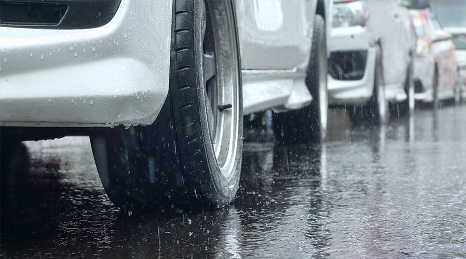 Un gros plan de pneus sur une route mouillée, illustrant comment prévenir les dommages à votre auto pendant une inondation.