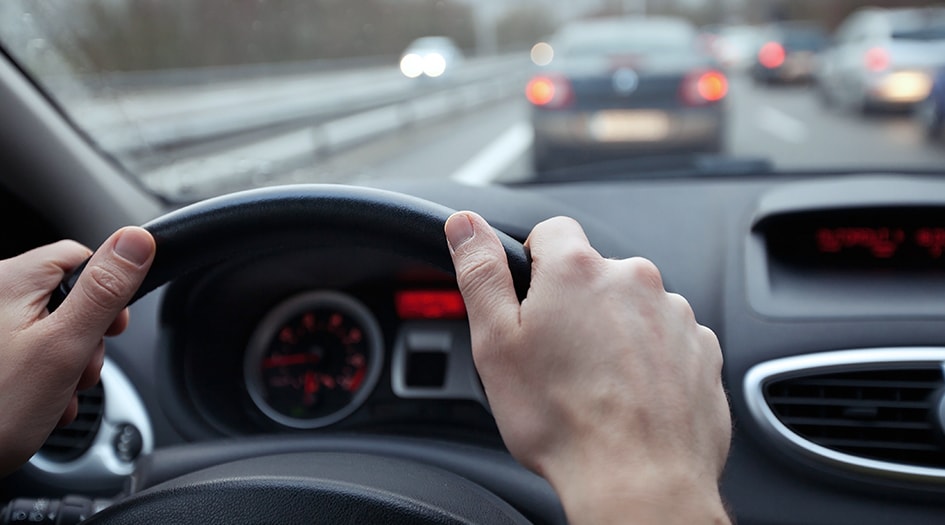 A close up on two hands on a car steering wheel shows how you can steer clear of insurance fraud and staged accidents