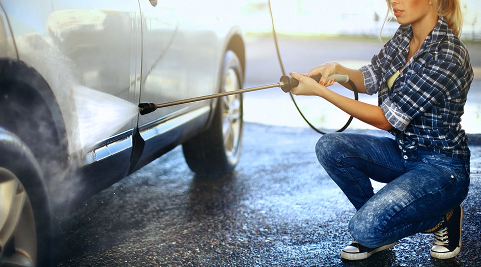 A woman uses a long hose extender to wash her car's tires, showing you one of the ways to get your vehicle ready for summer