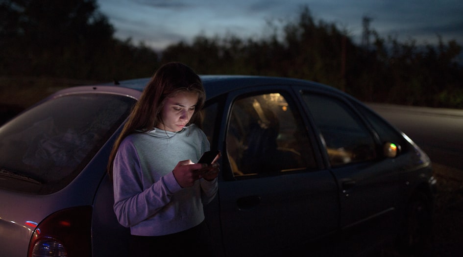 A woman is on her phone as she stands by her car in the dark, highlighting what to do if you get in a car accident outside business hours