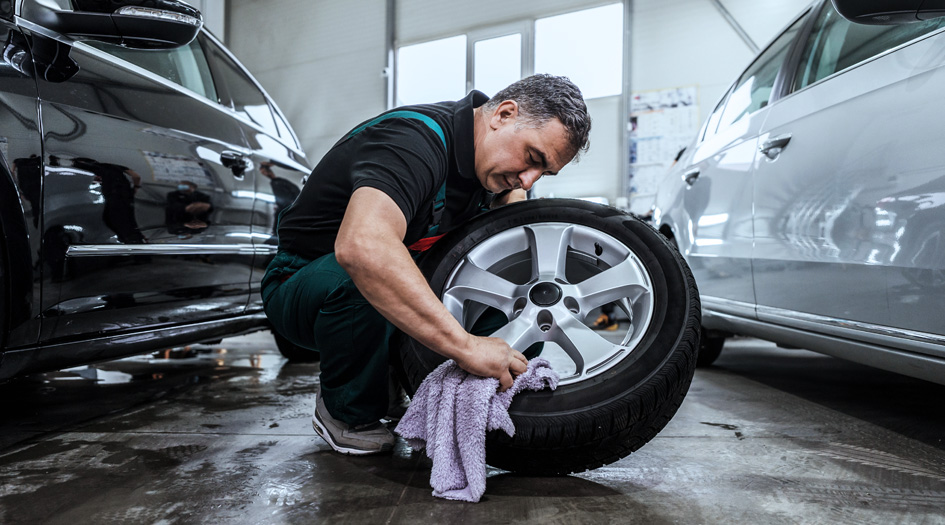 A man cleans the rims of a car’s tire, helping maintain and extend the car’s life.