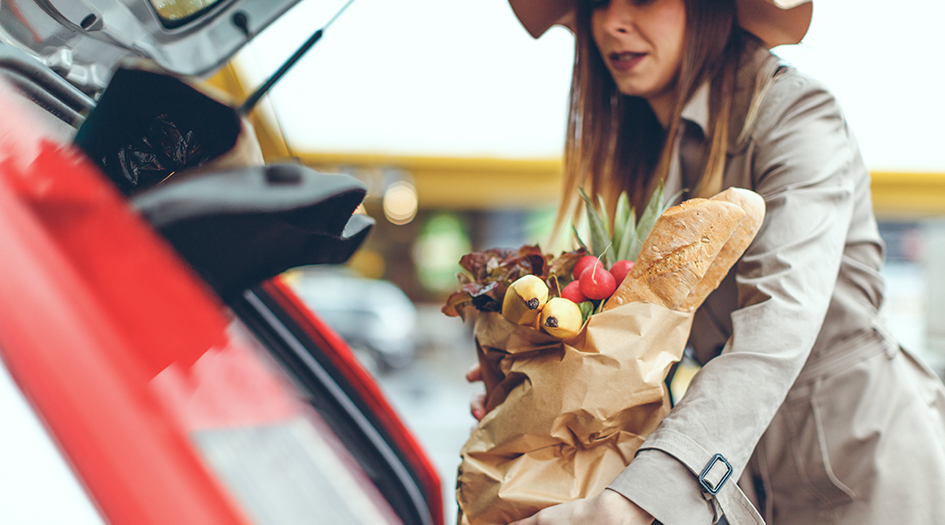 Une femme dépose des sacs d’épicerie dans le coffre de sa voiture, illustrant l’une des façons d’aider votre communauté.