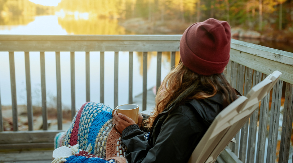 A woman sits on a porch and looks out at a lake, considering little-known facts about seasonal property insurance