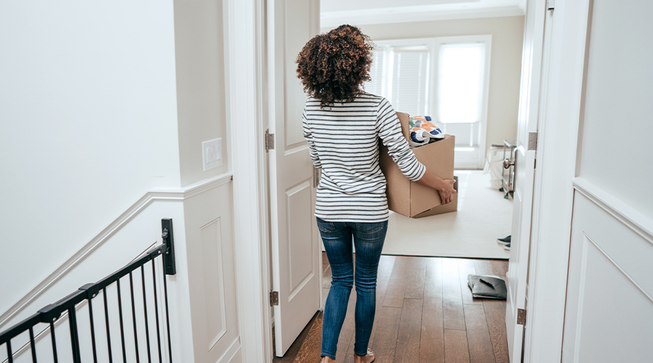 Une femme tient une boîte dans une pièce vide, illustrant les erreurs courantes des propriétaires sur l’assurance habitation.