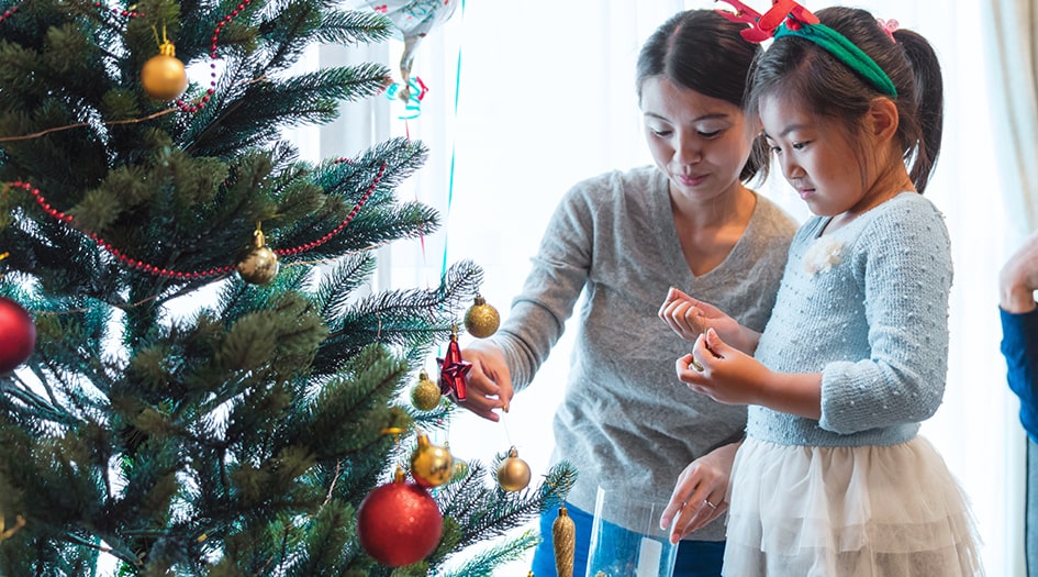 A woman and little girl decorate a Christmas tree, following to-dos off their Christmas decorating checklist