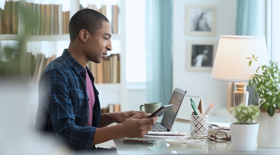 A man considers how a claim can affect his home insurance premium as he looks at his laptop and smartphone at a desk