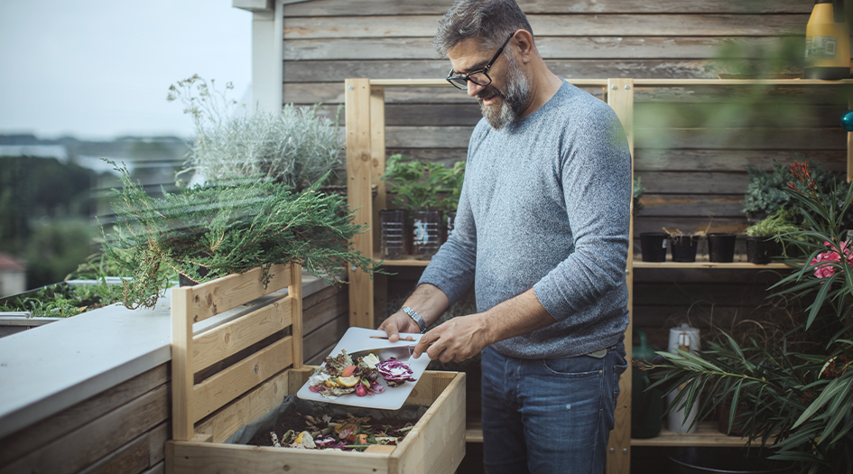 A man adds food to a compost bin, showing one way to be more eco-friendly at home