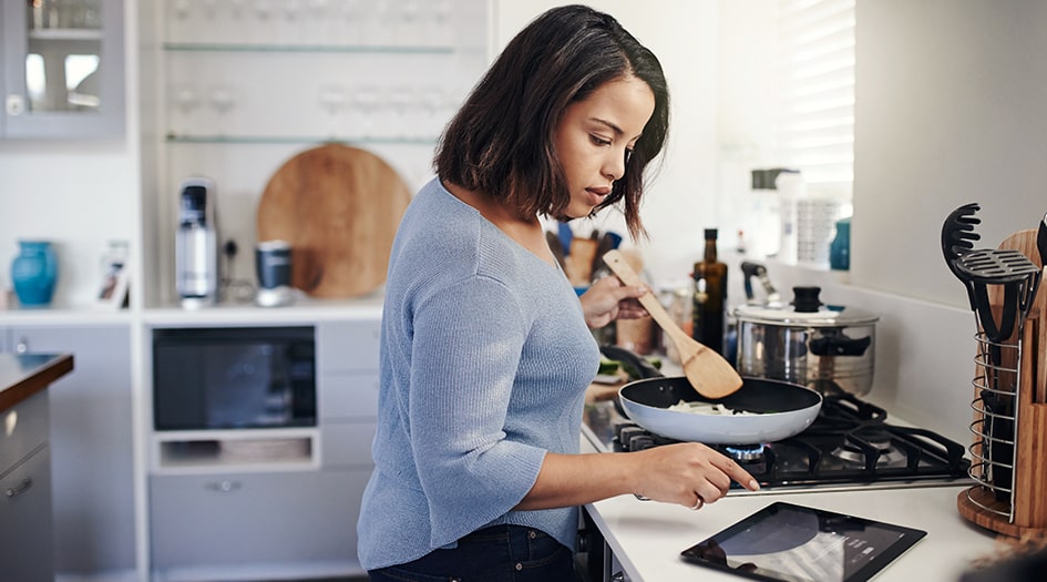 A woman consults a tablet while cooking on the stove, showing how to safeguard your home against fire