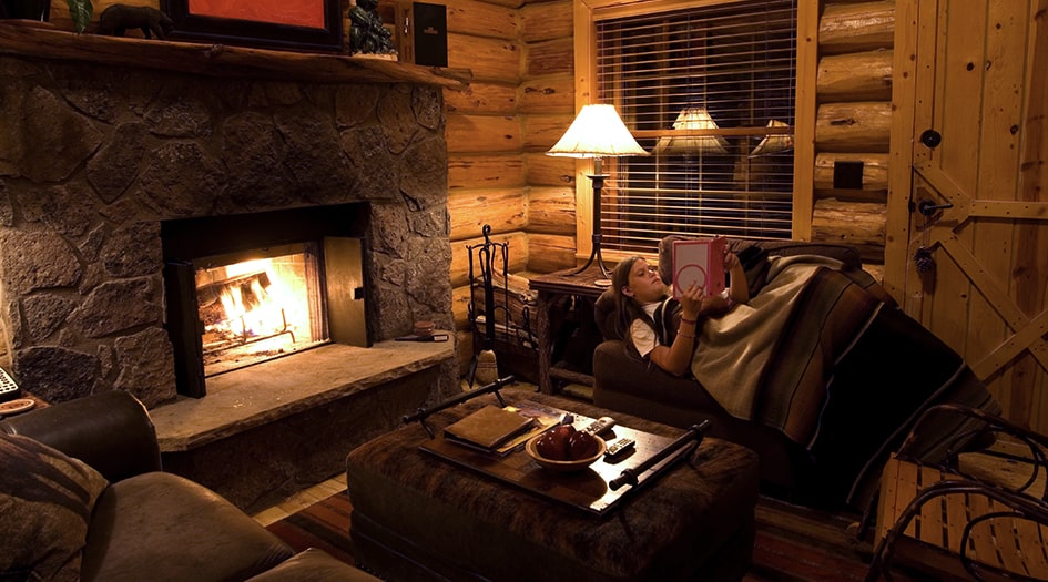 A woman lays on a couch, reading a book by a fireplace, showing how to safely use a wood burning fireplace