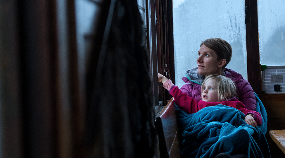 A woman and little girl sit together under a blanket and look out the window, showing you what to do before, during, and after a hailstorm