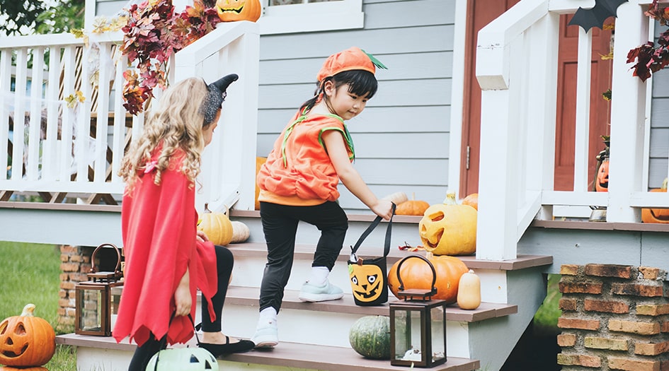 Two kids in costume walk up a decorated porch, highlighting how you should prepare your yard for a safe Halloween