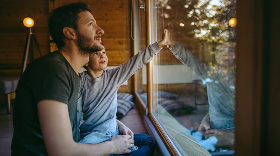 A man and child look out the window of their home, as they consider simple ways to save energy and lower heating bills in the winter 