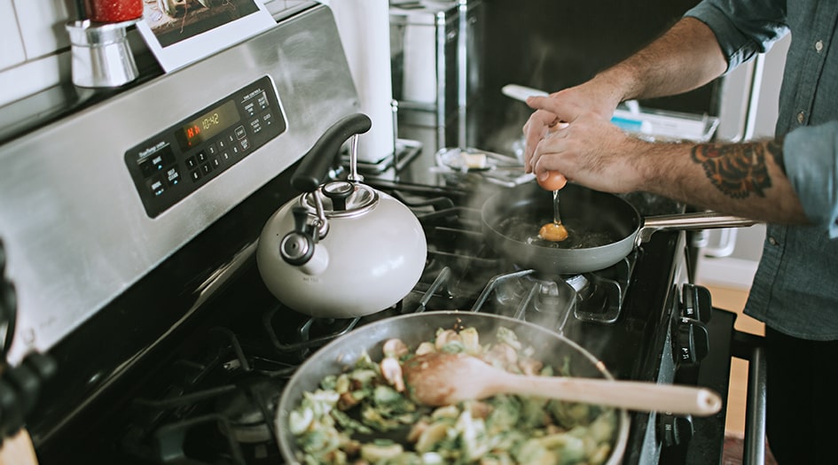 Un homme casse un œuf dans une poêle, illustrant quelques conseils pour prévenir et éteindre les incendies de cuisine.