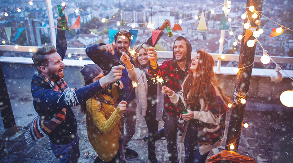 A group of people hold sparklers on a snowy rooftop, celebrating a safe and happy new year