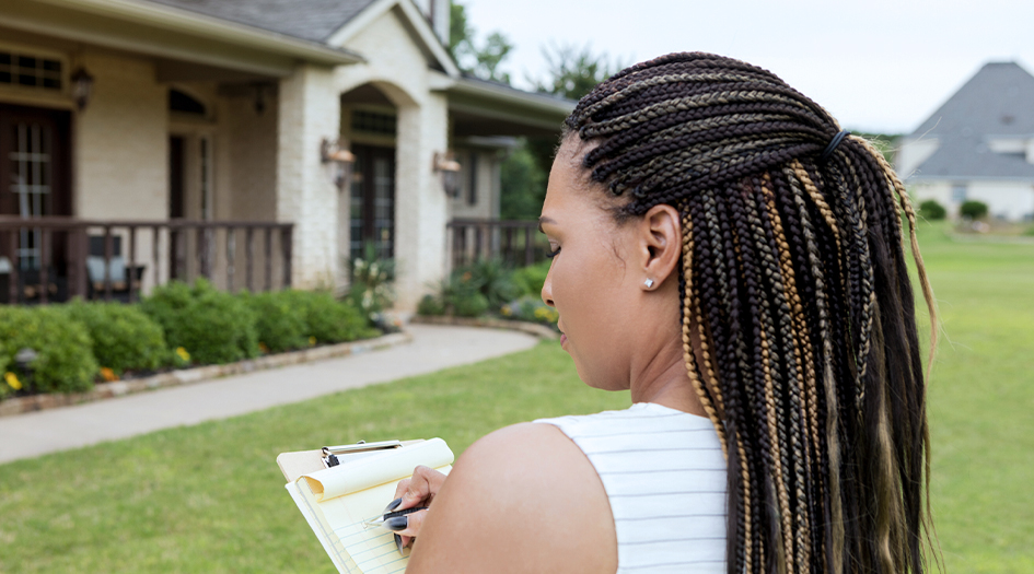 A woman prepares for an emergency at home while writing on a notepad on her front lawn