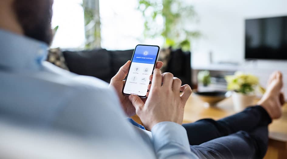 A man sits, looking at his phone, as he considers how to keep personal information secure while using smart home devices