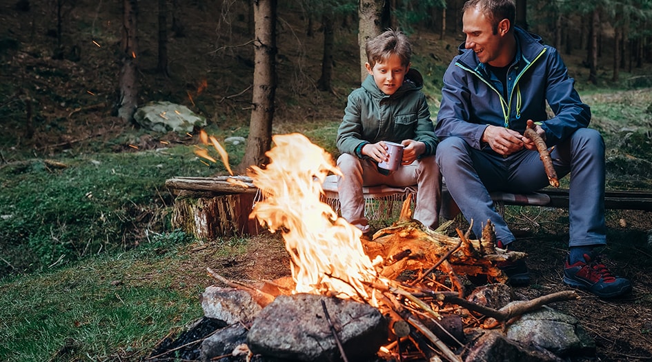 A man and boy sit on a bench in front of a bonfire, showing some simple ways to help prevent wildfires