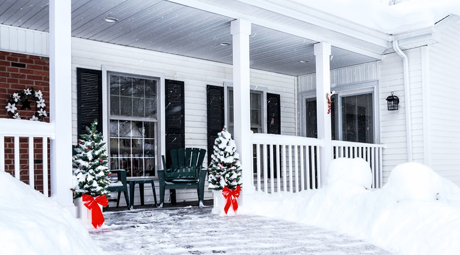 A house's porch is decorated for the holidays while snow falls, showing how you can get your house ready for winter