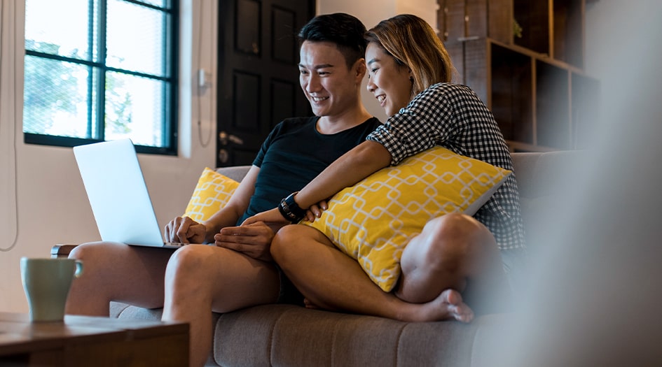 Un homme et une femme sont assis sur le sofa devant un ordinateur portable et découvrent l’assurance Umbrella.