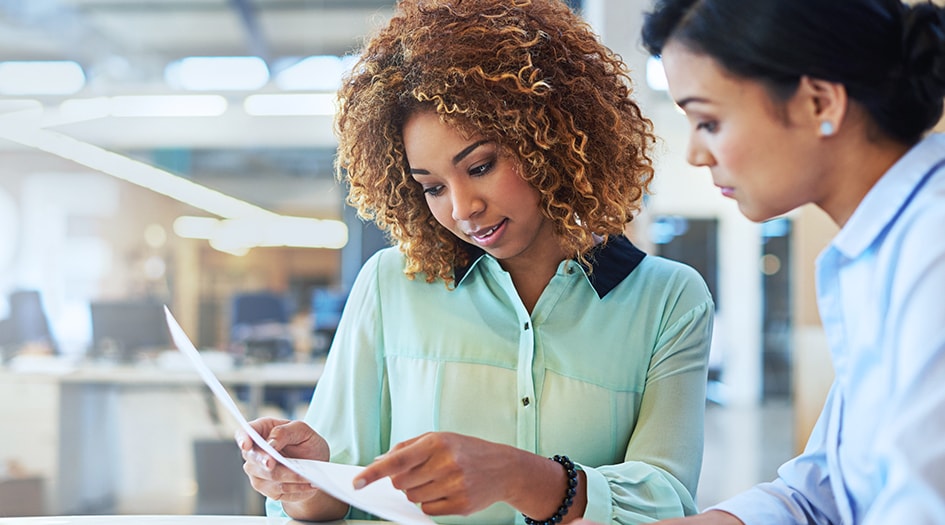 Two women analyze a piece of paper, learning how insurance works