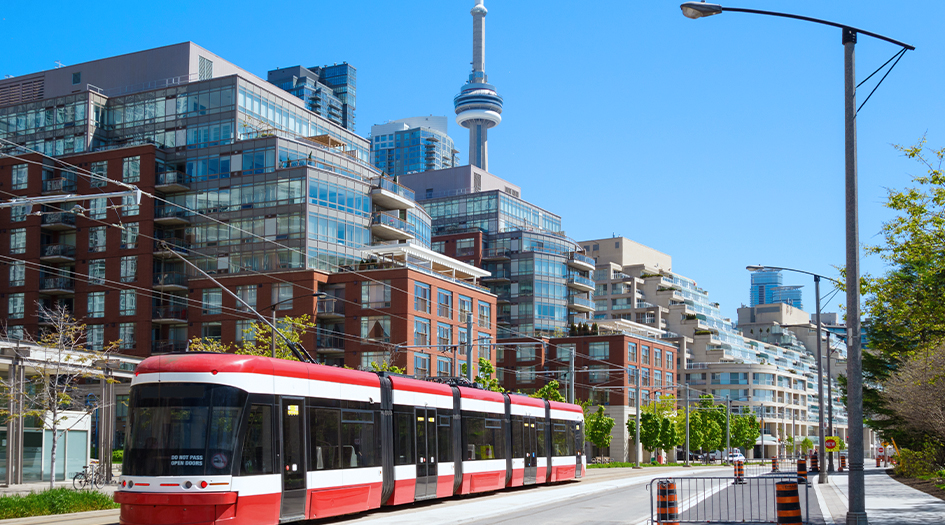 A streetcar goes by a row of buildings with the CN Tower in the back, showing how your location affects the cost of your insurance