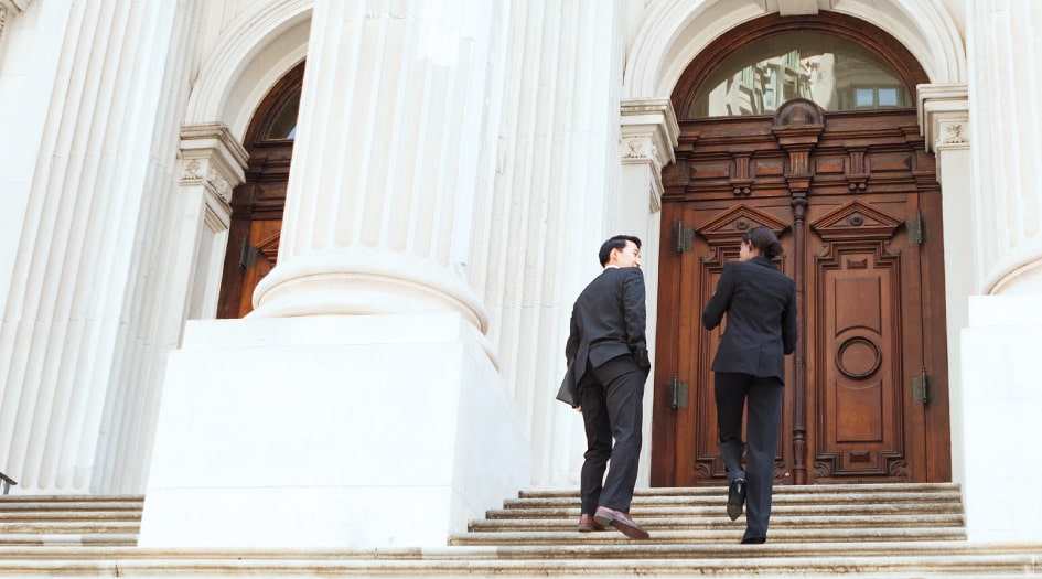 Deux personnes discutent de ce qu’est l’assurance responsabilité civile en montant les marches d’un édifice gouvernemental.