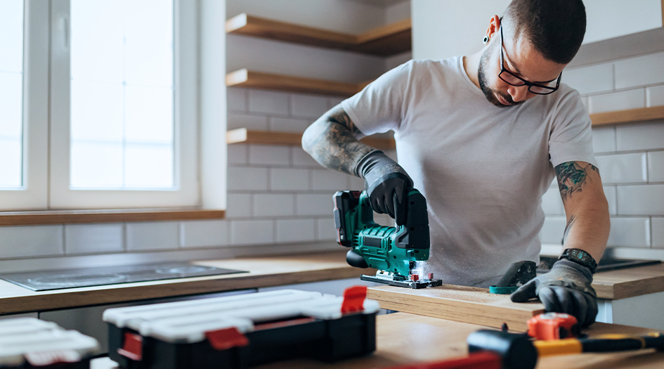 A man uses a saw to cut wood in a kitchen, showing one home renovation that can increase your home’s property value